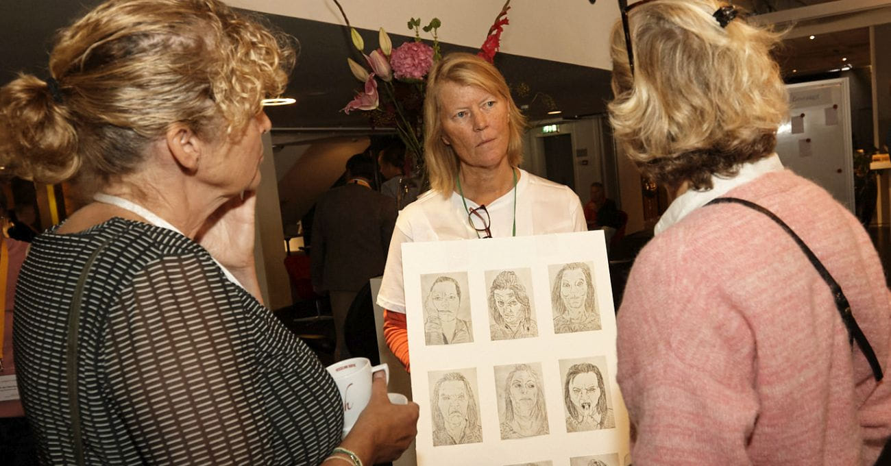 Organisatieadviseur Jolanda van Dijk draagt een bord met getekende gezichten en gaat hierover in gesprek met congresdeelnemers