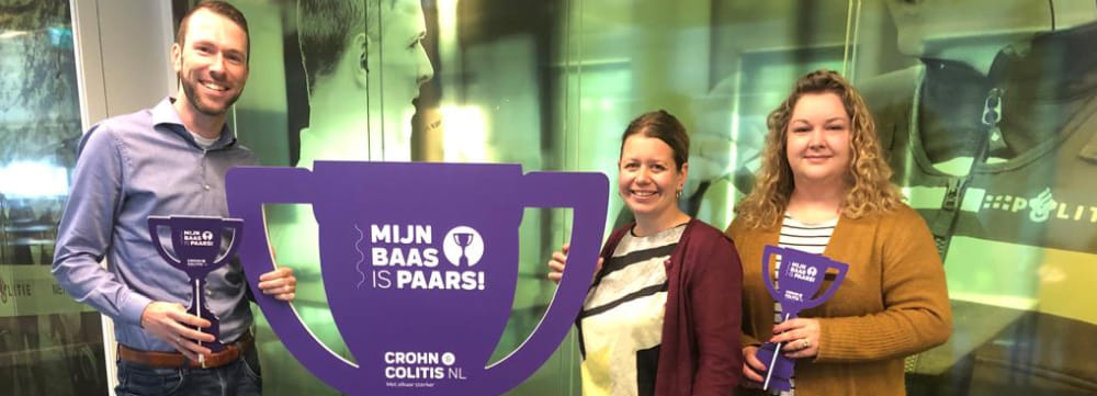 2 politiemedewerkers reiken de 'Mijn baas is paars-supertrofee' uit aan hun werkgever